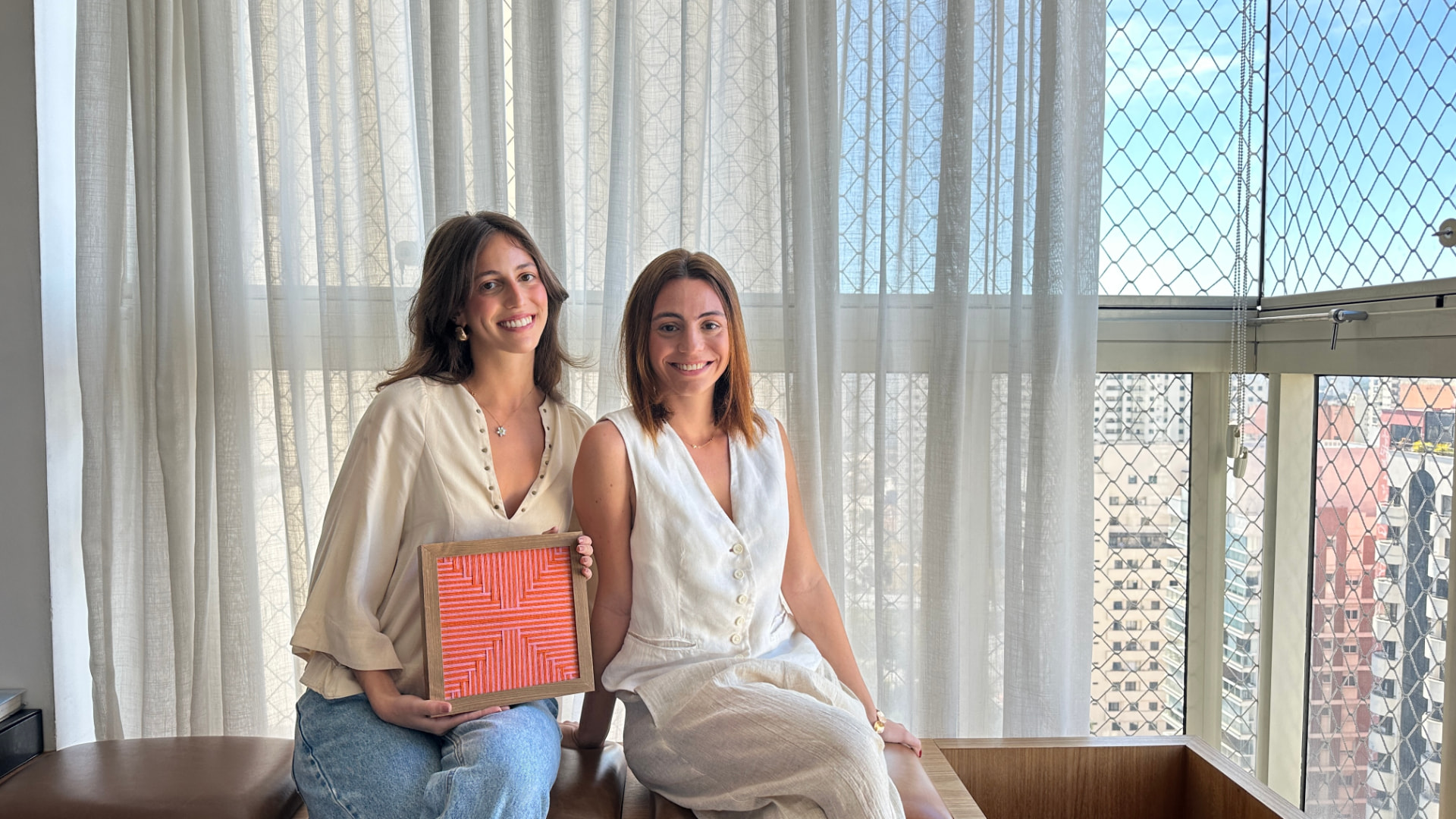 Fundadoras da Ato Studio com uma peça têxtil emoldurada